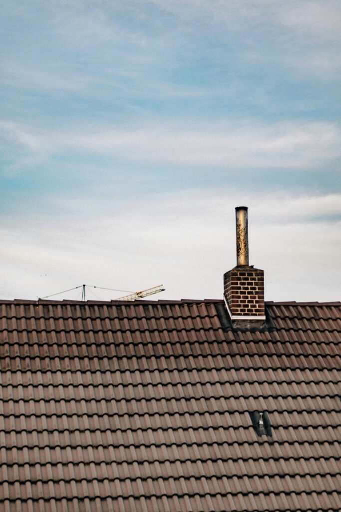 A brick chimney on a brown tile roof under a tranquil, cloud-filled sky.